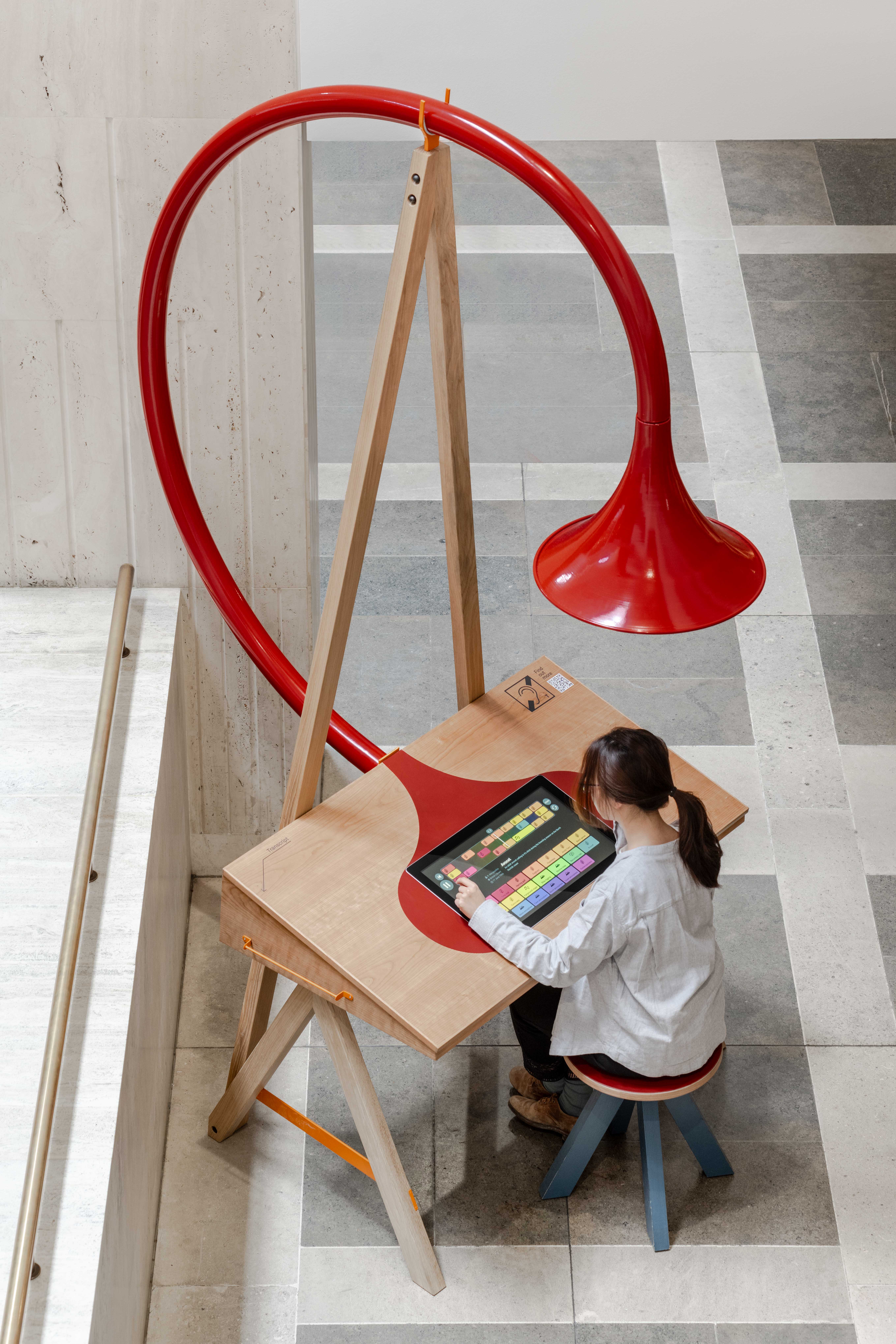 Image of Emily Peasgood's Listening Desk in The British Library. A young woman is sat at the desk, playing with the interactive screen. A large horn is above her head.