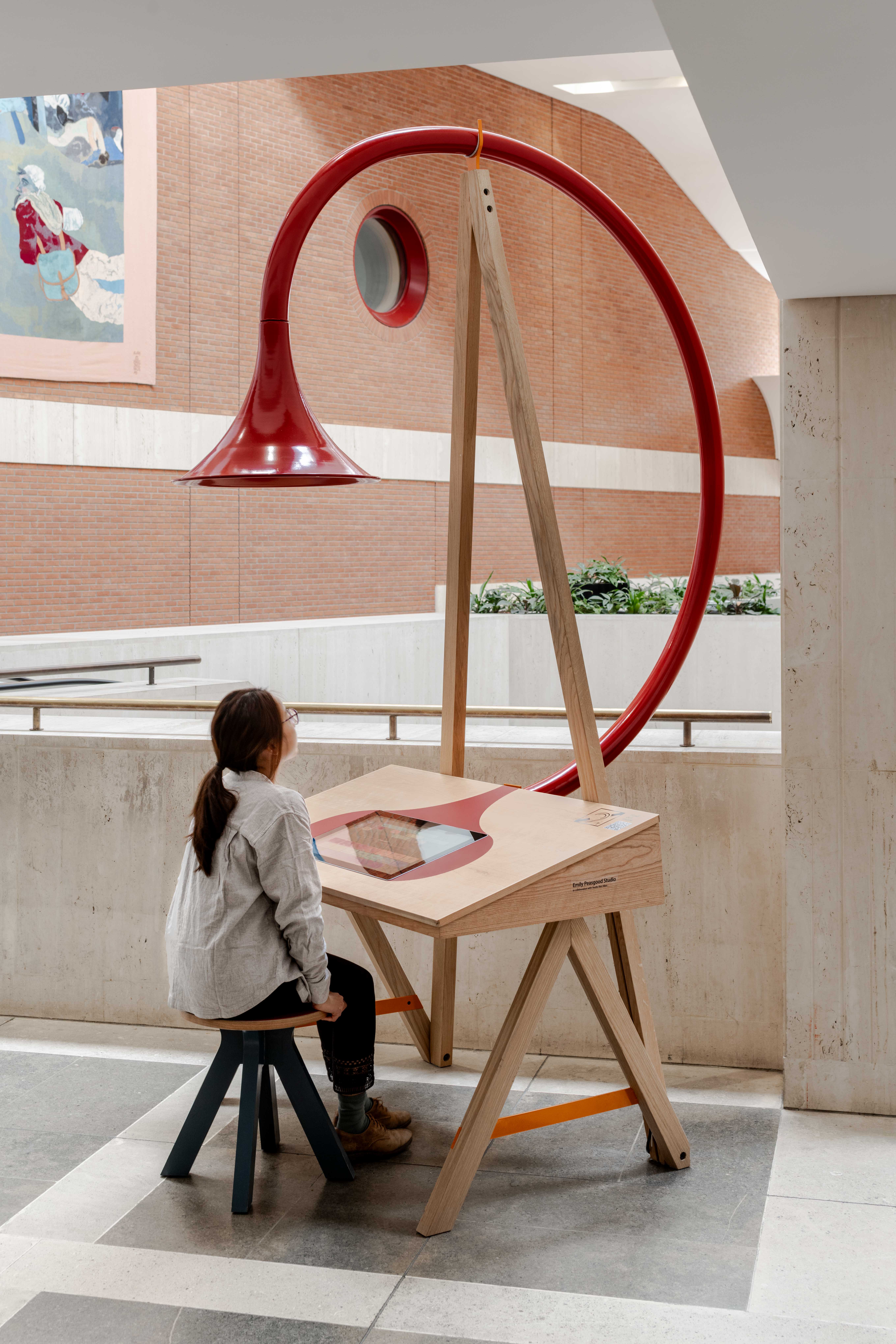 Image of Emily Peasgood's Listening Desk in The British Library. A young woman is sat at the desk, playing with the interactive screen. A large horn is above her head.