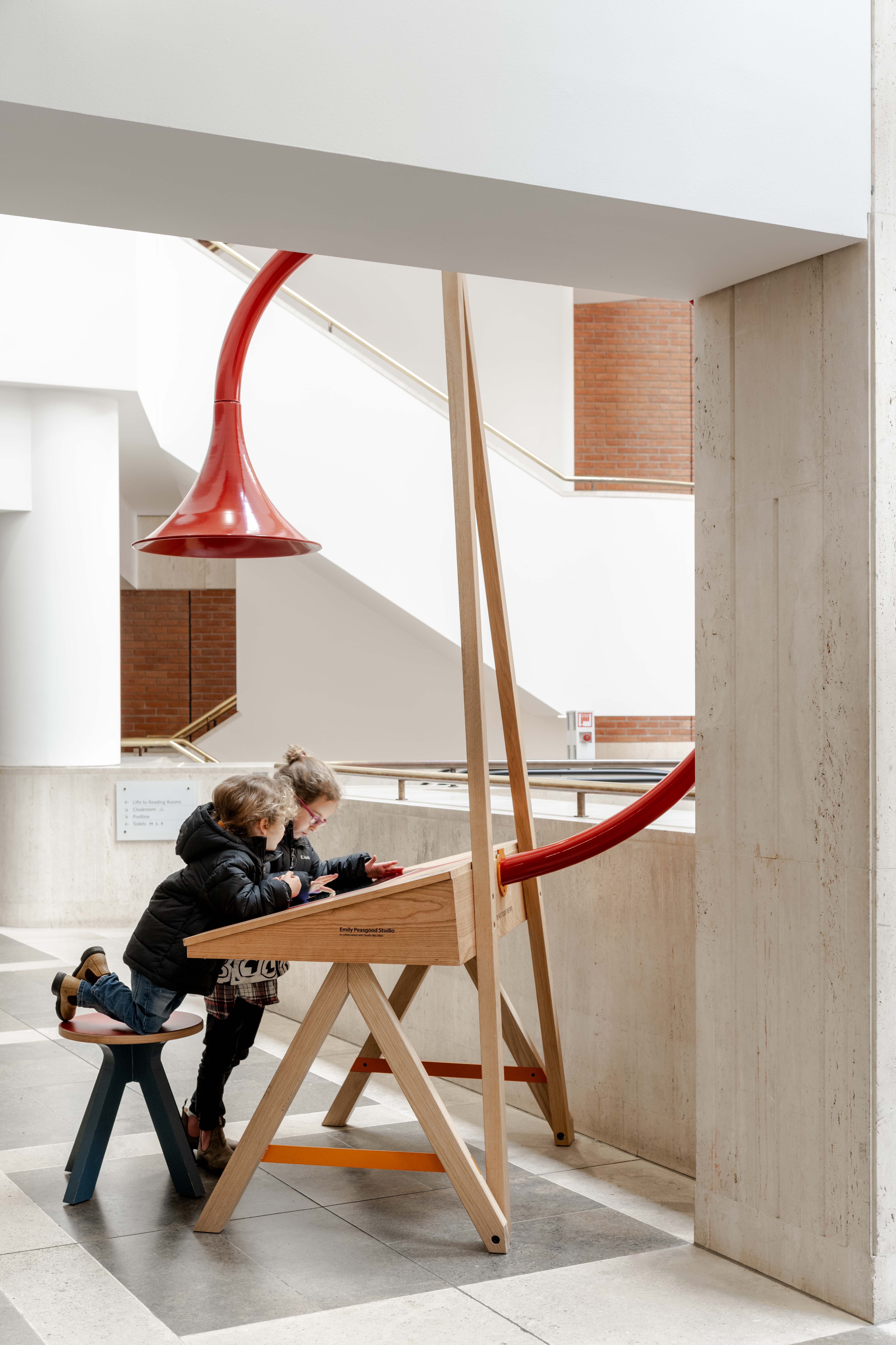 Image of Emily Peasgood's Listening Desk in The British Library. Two children are sat at the desk, playing with the interactive screen. A large horn is above their heads.