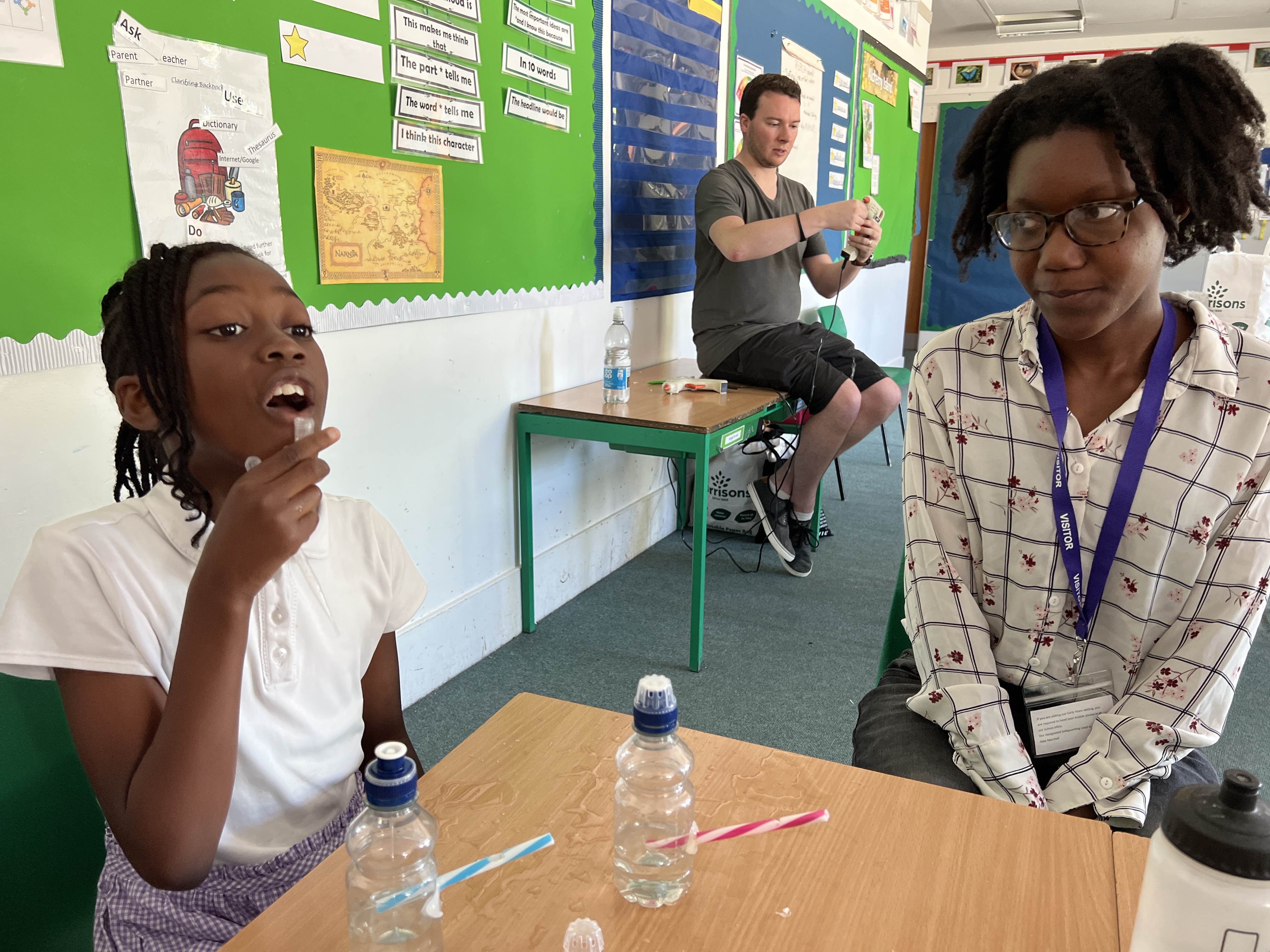 This image shows two teachers sitting with a Year 4 student who is blowing a bird whistle they made.