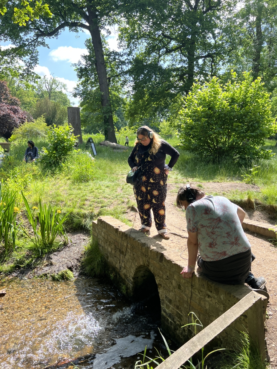 Sounds of the Subaquatic in The Royal Parks, London, led by sound artist Emily Peasgood, 2023. Emily Peasgood and Sam Slattery (guest artist) are looking at a stream in Bushy Park and discussing how to record it.