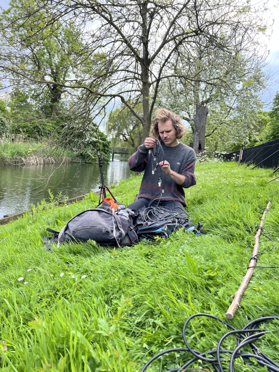 Sounds of the Subaquatic in The Royal Parks, London, led by sound artist Emily Peasgood, 2023. Geoffrey Papin (assistant field recordist) is sat on the banks of Queen Mary's Garden Pond in The Regents Park. He is untangling some hydrophone cables.