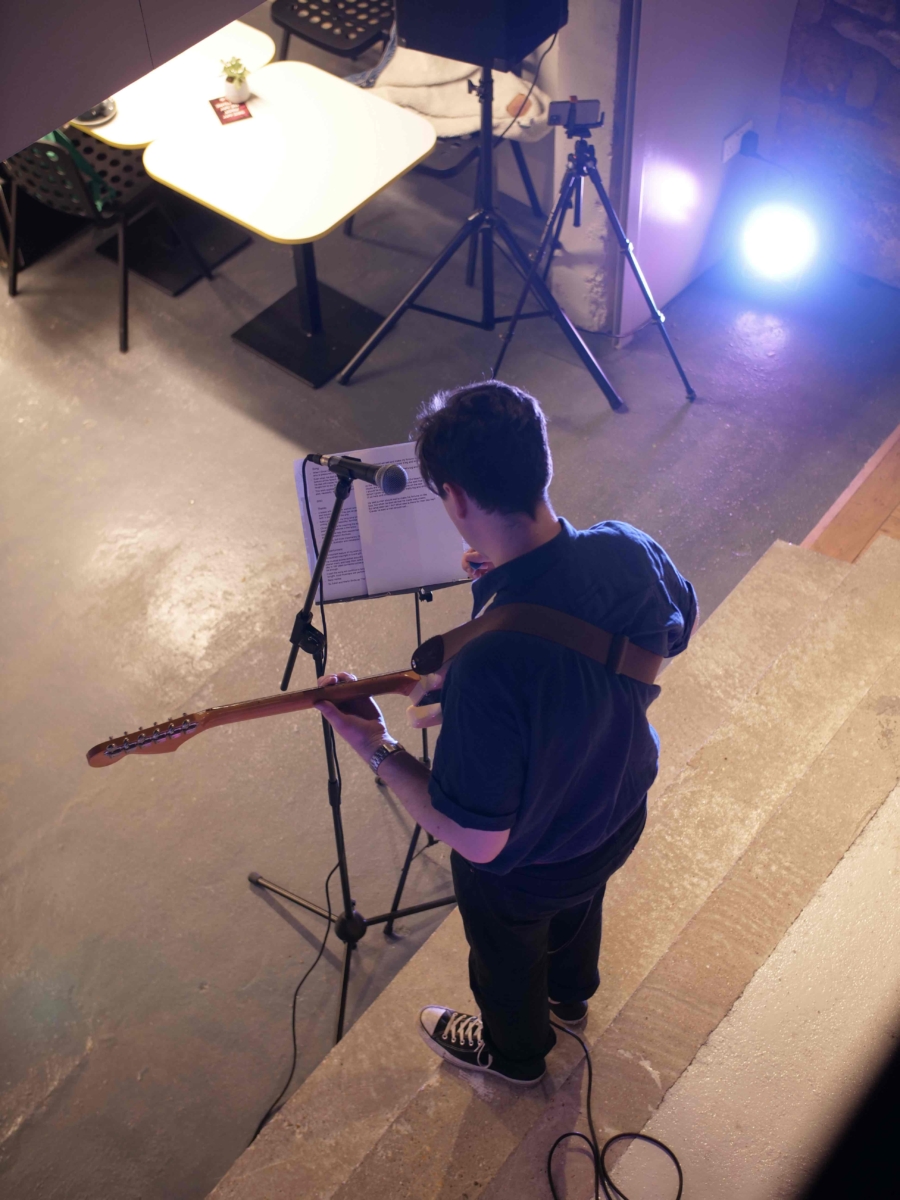 Musician Benji Heinke is playing his interpretation of 'When I Grow Up I Want To Be A Ship' at the launch event. The photo is taken from above and Benji is playing guitar and looking at some music on a music stand. 