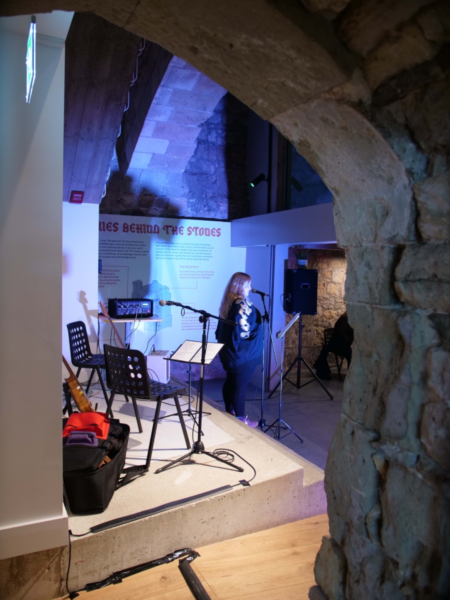 Emily Peasgood is giving her opening speech in the bar of God's House Tower at the launch of When I Grow Up I Want To Be A Ship in 2022. The photo is taken from the side and only Emily is in shot. The stage is in the background.