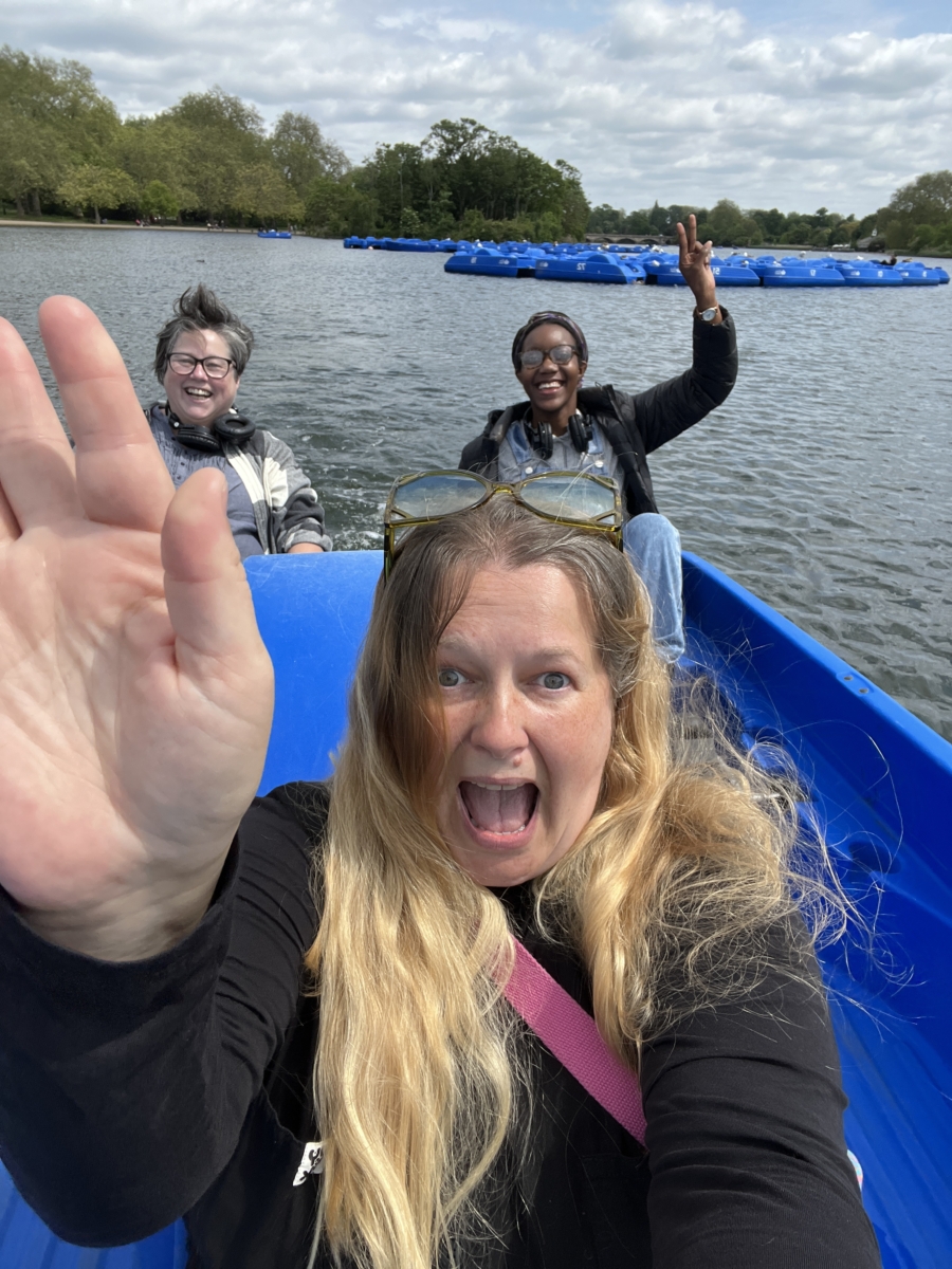Sounds of the Subaquatic in The Royal Parks, London, led by sound artist Emily Peasgood, 2023. Emily Peasgood, Vicki Salmi (guest artist) and Dani Osoba (assistant field recordist) are sat in a pedalo in The Serpentine at Hyde Park. They are laughing and waving at the camera.
